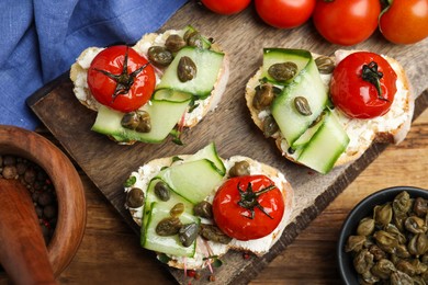 Photo of Bruschettas with capers, vegetables and cream cheese served on wooden table, flat lay