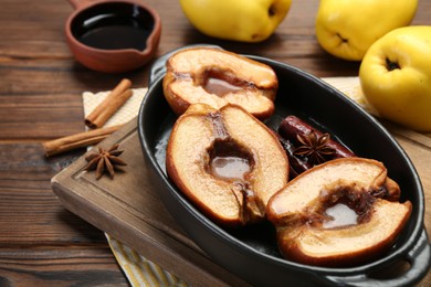 Tasty baked quinces with spices and honey in dish on wooden table, closeup
