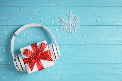 Photo of Modern headphones and gift box on blue wooden background, top view with space for text. Christmas music concept