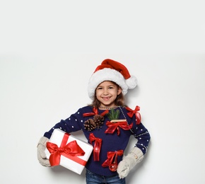 Photo of Cute little girl in handmade Christmas sweater and hat holding gift on white background