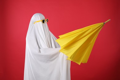 Photo of Person in ghost costume and sunglasses holding yellow umbrella on red background