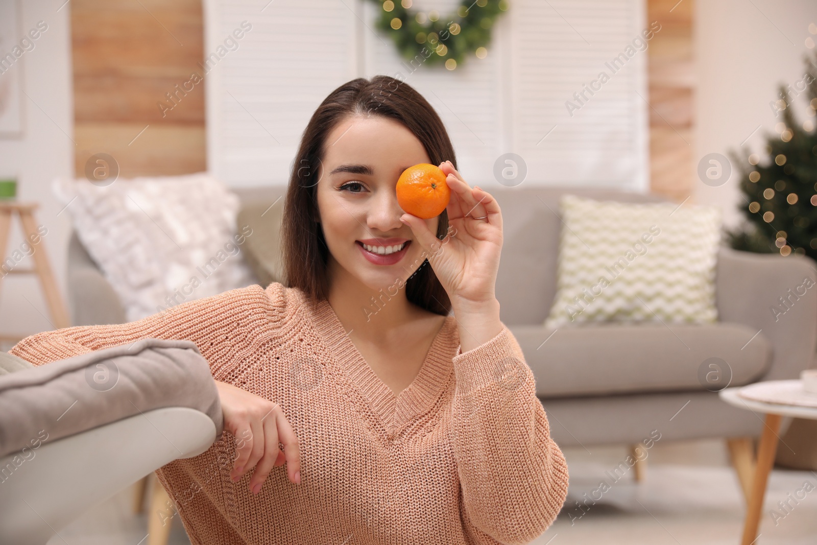 Photo of Happy young woman with tangerine in living room