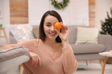 Happy young woman with tangerine in living room