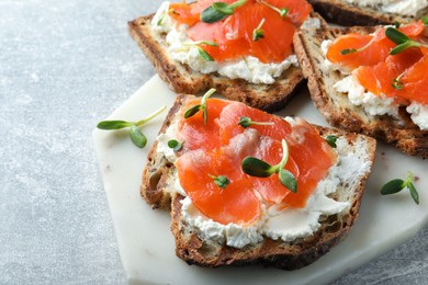 Delicious sandwiches with cream cheese, salmon and microgreens on light grey table, closeup