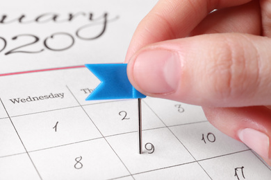 Photo of Woman marking date in calendar with drawing pin, closeup