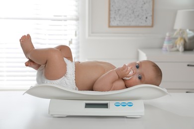 Photo of Cute little baby lying on scales at home