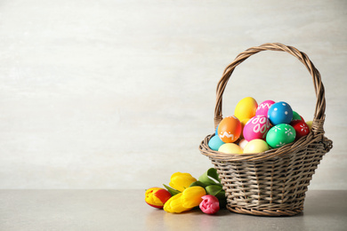 Basket with colorful Easter eggs and tulip flowers on light grey background. Space for text