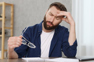 Photo of Overwhelmed man sitting with glasses at table indoors