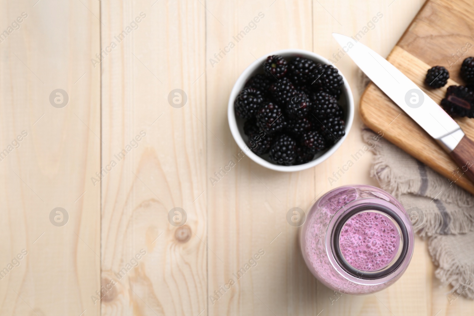 Photo of Delicious blackberry smoothie in glass bottle and fresh berries on wooden table, flat lay. Space for text