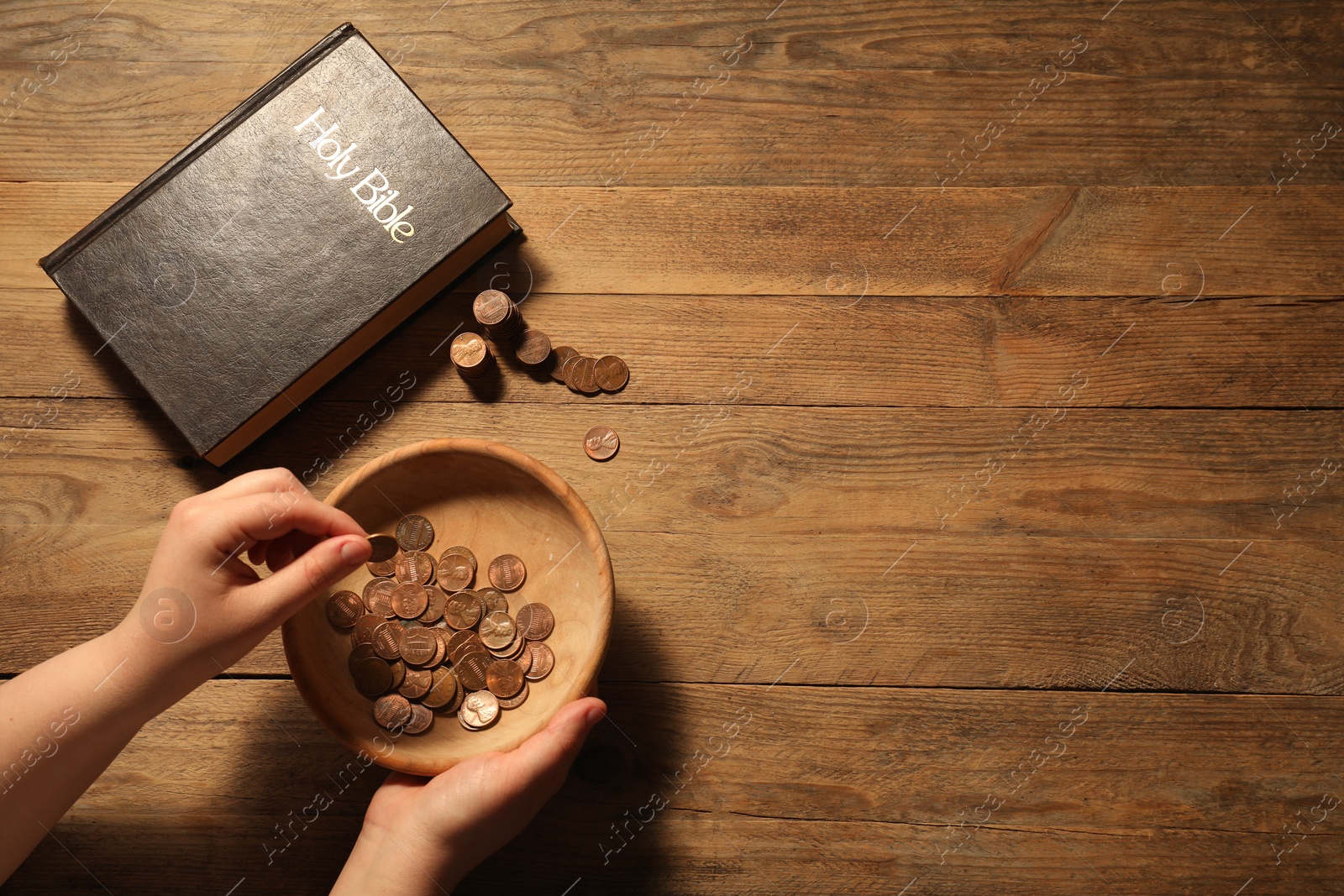 Photo of Donate and give concept. Woman putting coin into bowl at wooden table, top view. Space for text