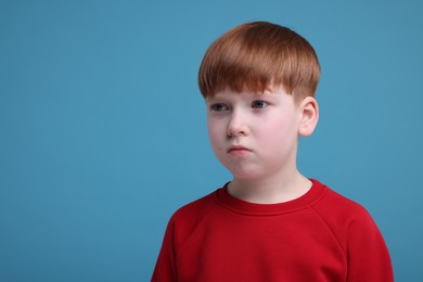 Portrait of sad little boy on light blue background, space for text