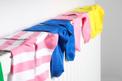 Photo of Different colorful socks on heating radiator near white wall, closeup