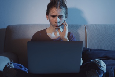Photo of Upset teenage girl with laptop on sofa in dark room. Danger of internet