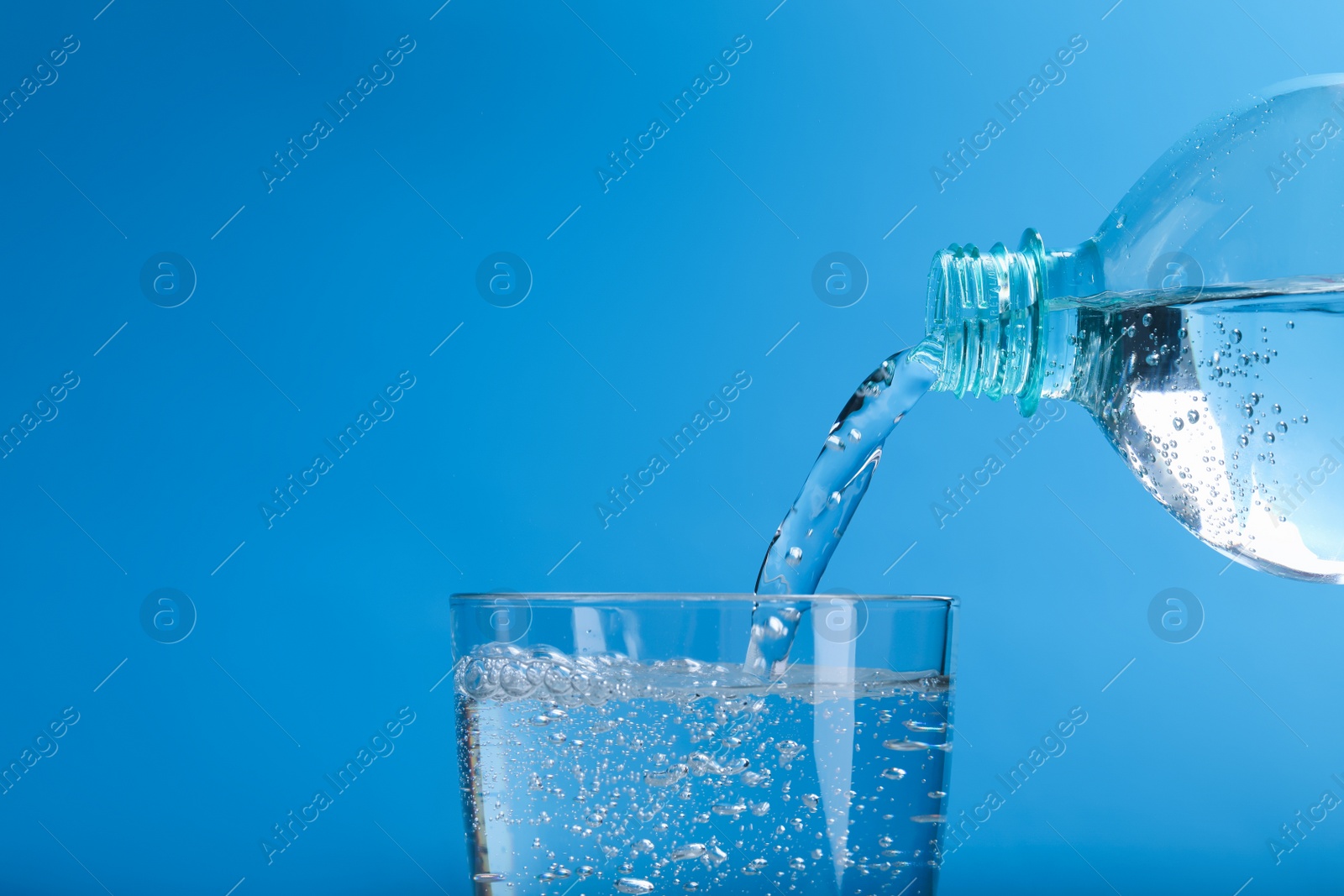 Photo of Pouring soda water from bottle into glass on light blue background, closeup. Space for text