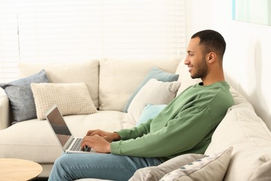 Photo of African American man typing on laptop on sofa in room