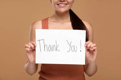 Photo of Woman holding card with phrase Thank You on brown background, closeup