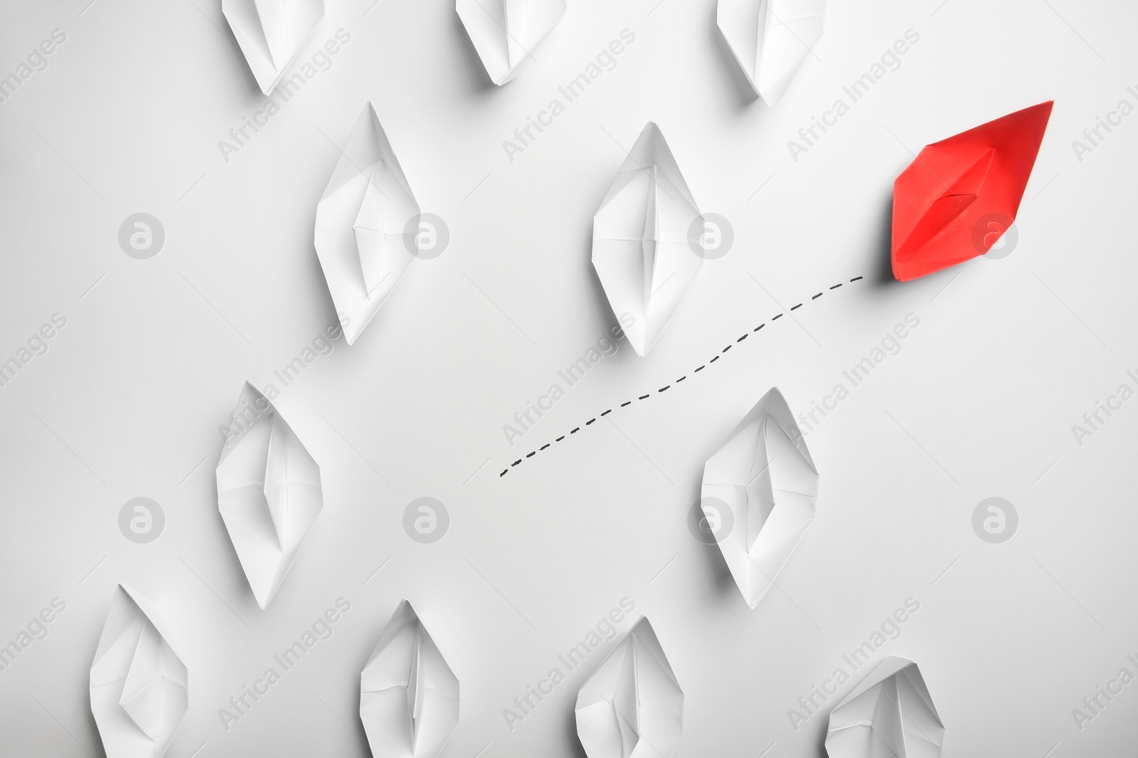 Photo of Red paper boat floating away from others on white background, flat lay. Uniqueness concept