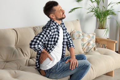 Man suffering from pain in back on sofa at home