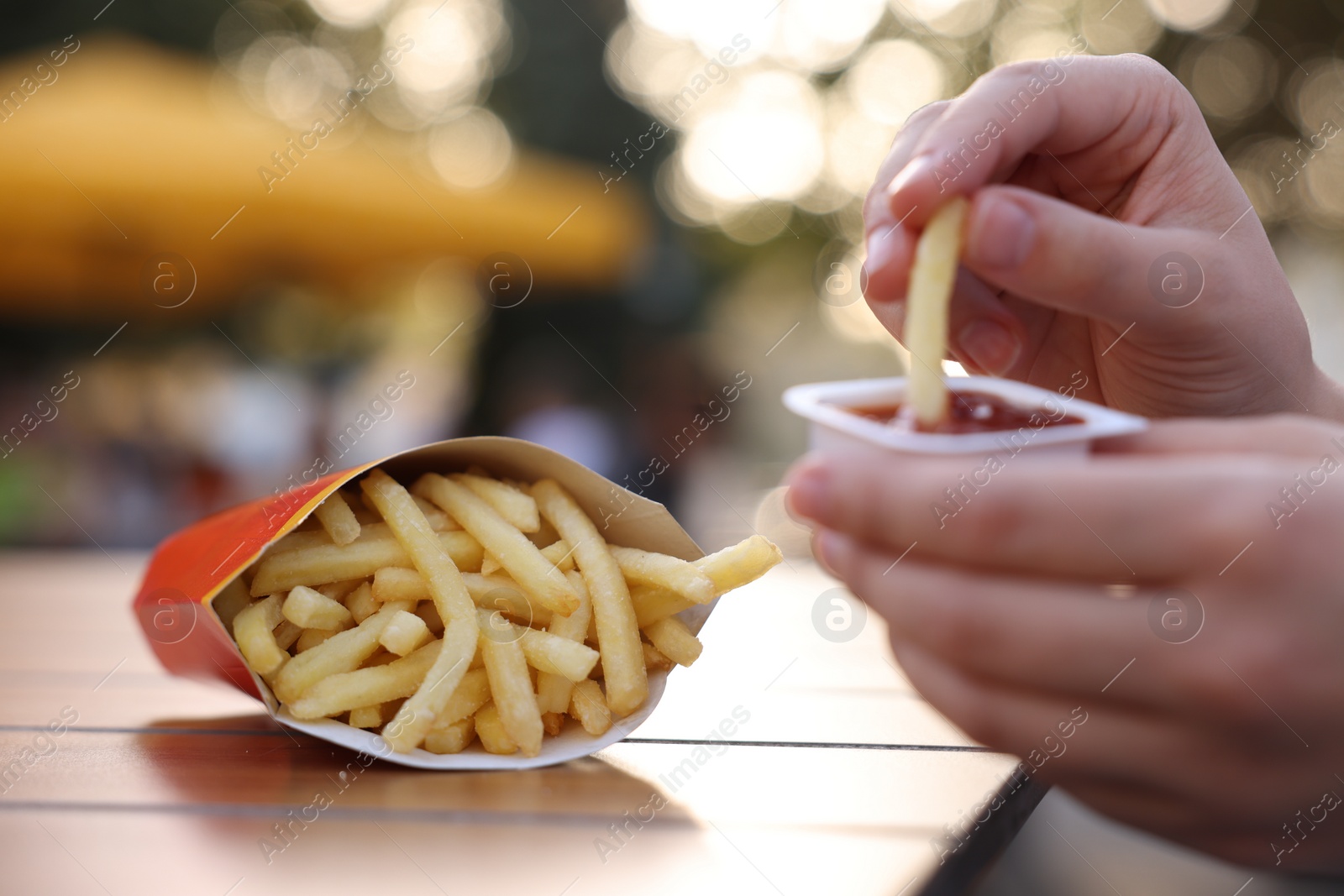 Photo of Lviv, Ukraine - September 26, 2023: Woman dipping McDonald's french fry into sauce at wooden table outdoors, selective focus