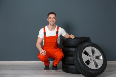 Young mechanic in uniform with car tires near dark wall