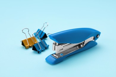Photo of New bright stapler with binder clips on light blue background. School stationery
