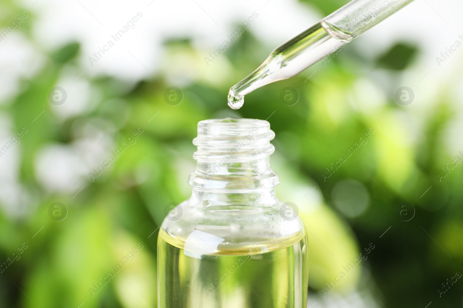 Photo of Dropper with essential oil over bottle against blurred background, closeup