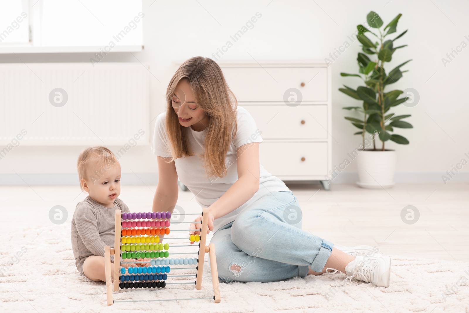 Photo of Children toys. Happy mother and her little son playing with wooden abacus on rug at home