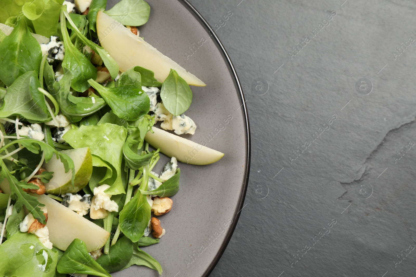 Photo of Tasty salad with pear slices on black table, top view. Space for text