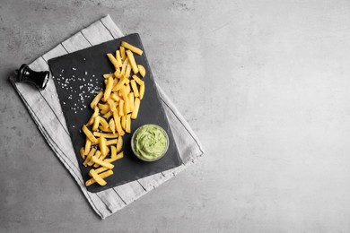 Photo of Serving board with french fries and avocado dip on grey table, top view. Space for text