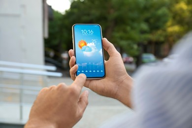Image of Man checking weather using app on smartphone outdoors, closeup. Data and illustration of sun with cloud on screen