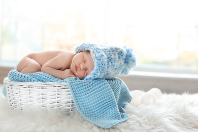 Photo of Adorable newborn baby lying in basket with knitted plaid indoors