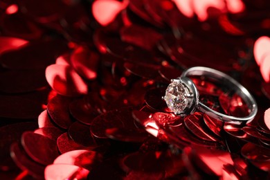 Photo of Beautiful engagement ring on red shiny paillettes, closeup. Space for text