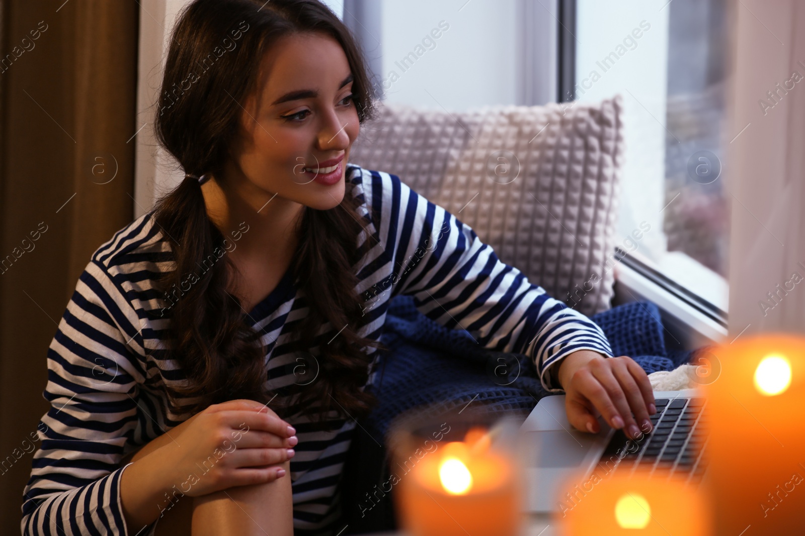 Photo of Young woman using laptop near window at home. Winter atmosphere