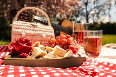 Photo of Delicious food, wine and picnic basket on blanket in park