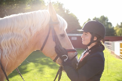 Photo of Young woman in horse riding suit and her beautiful pet outdoors on sunny day