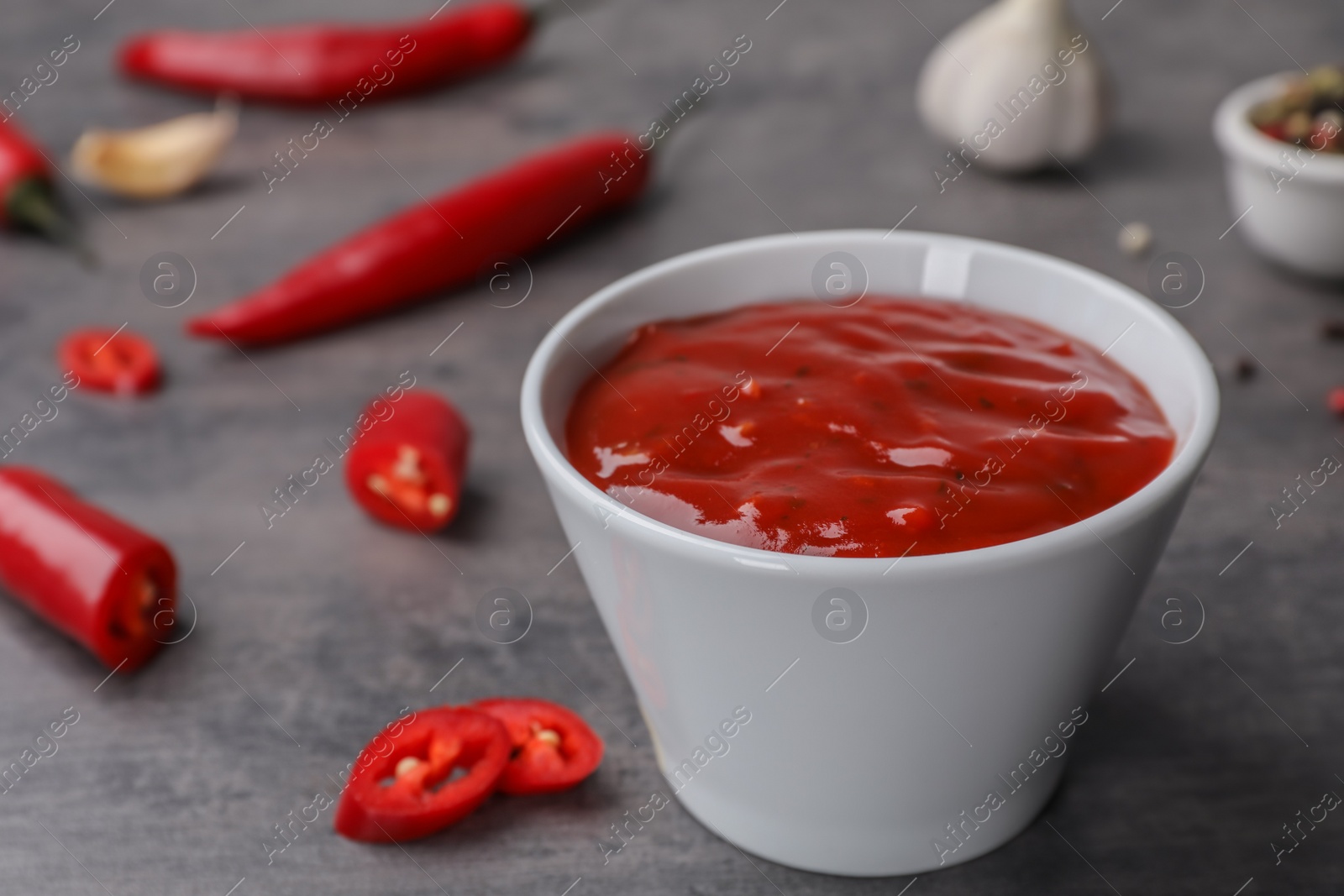 Photo of Bowl with hot chili sauce on gray table