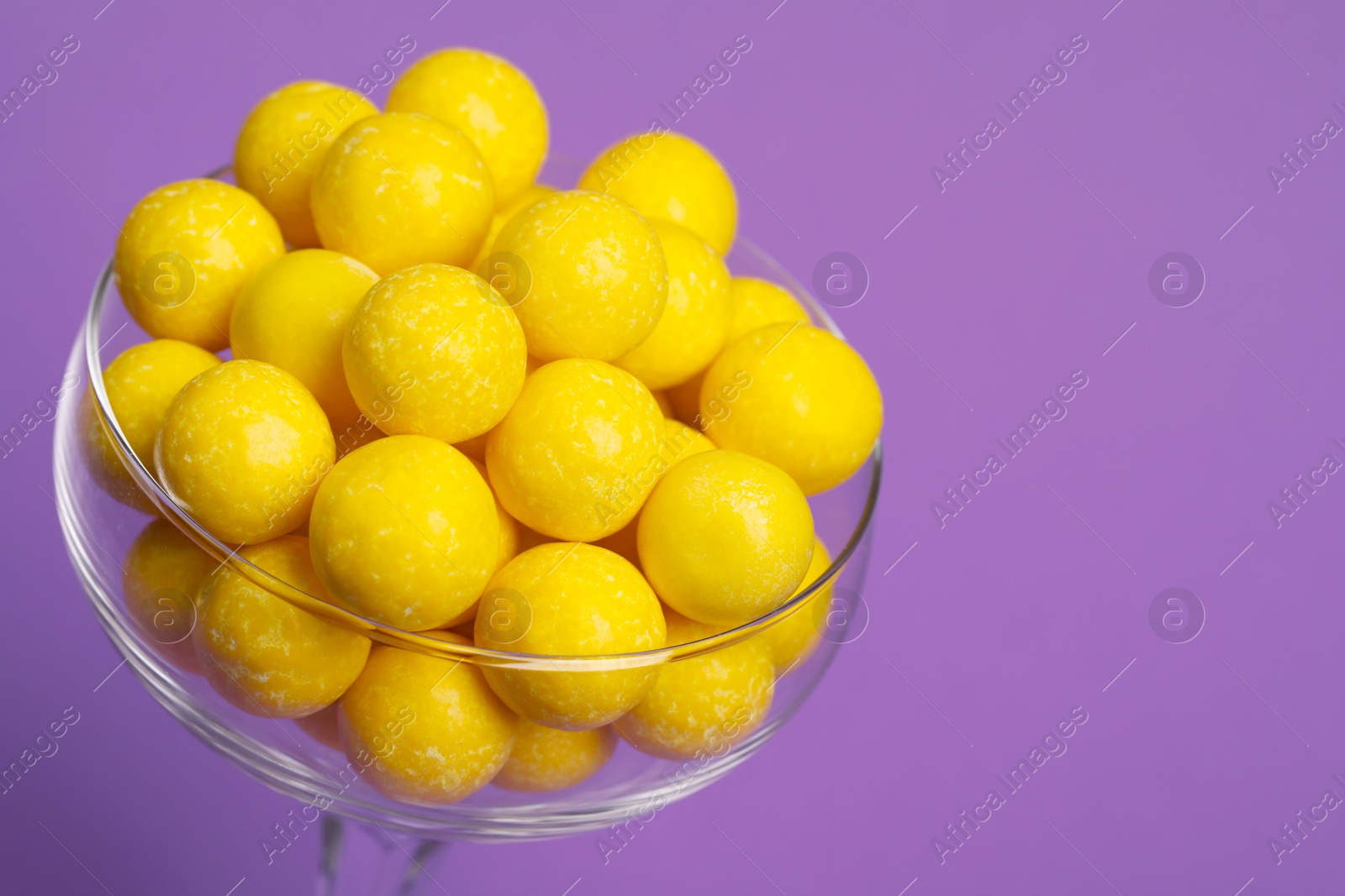 Photo of Tasty lemon chewing gums in glass on purple background, closeup