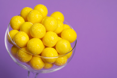 Tasty lemon chewing gums in glass on purple background, closeup