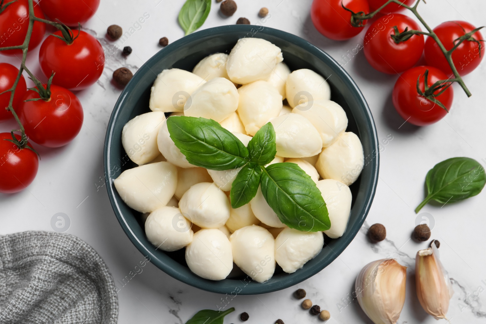 Photo of Delicious mozzarella balls in bowl, tomatoes and basil leaves on white marble table, flat lay