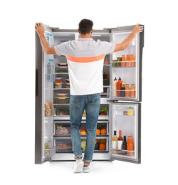 Photo of Man near open refrigerator on white background, back view