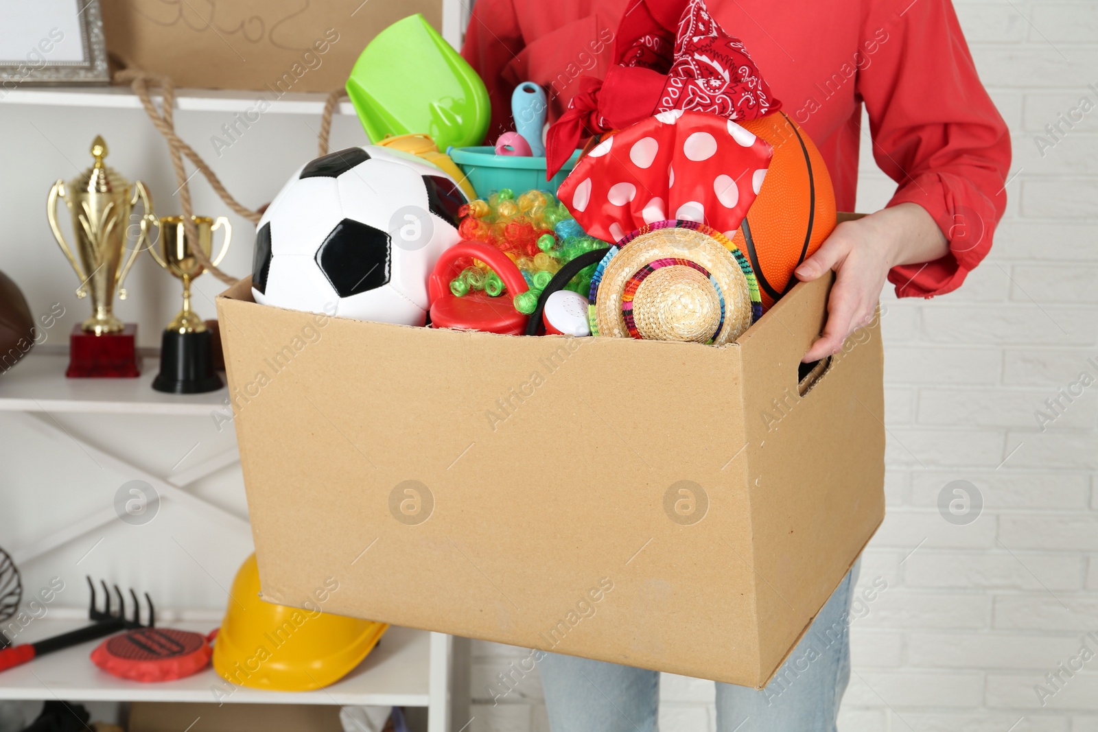 Photo of Woman holding box of unwanted stuff indoors, closeup