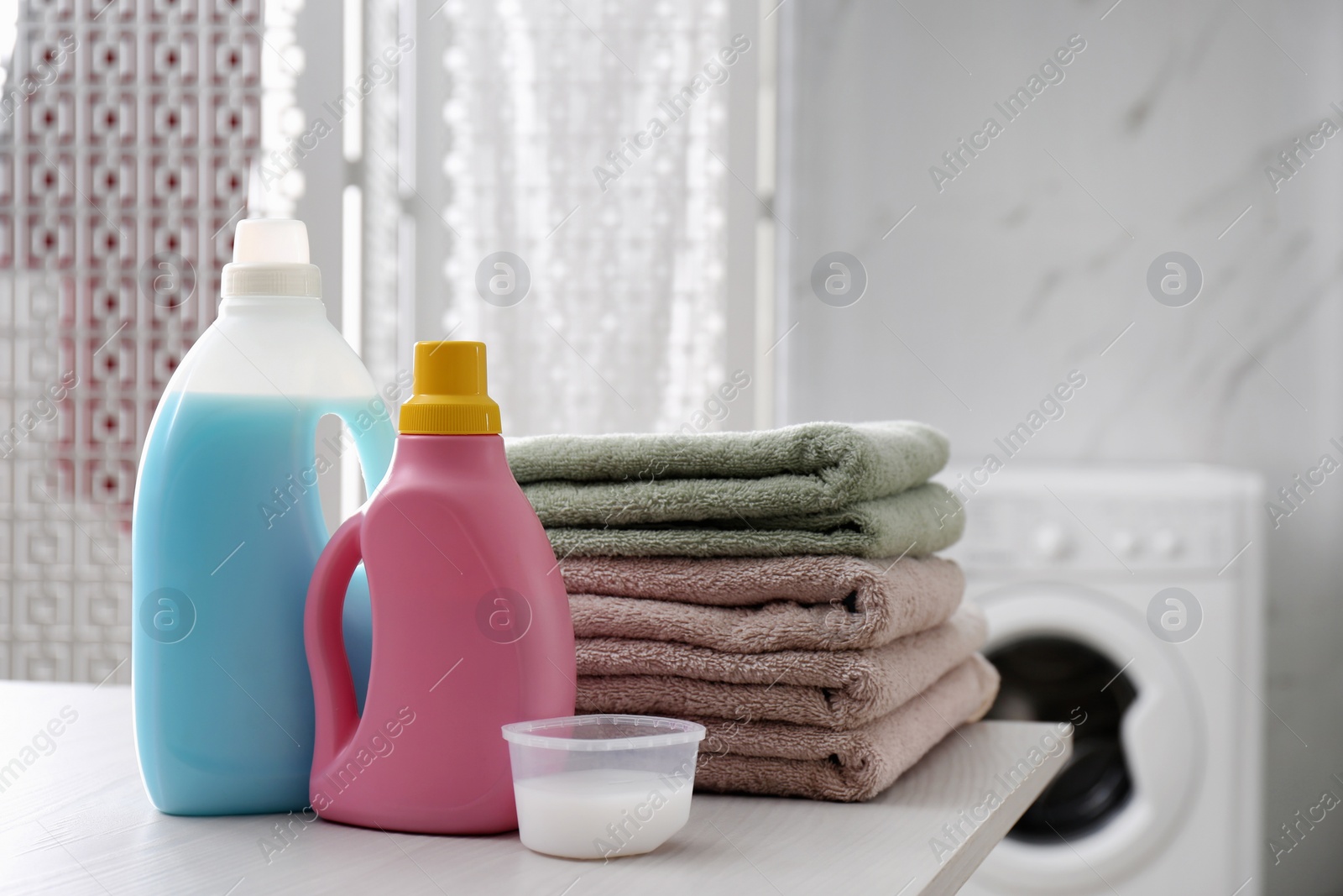 Photo of Stack of folded towels and detergents on white table in bathroom