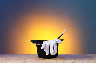 Photo of Magician's hat, wand and gloves on wooden table against color background