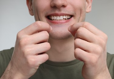Young man with whitening strip on light grey background, closeup