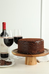 Photo of Delicious truffle cake, chocolate pieces and red wine on light wooden table