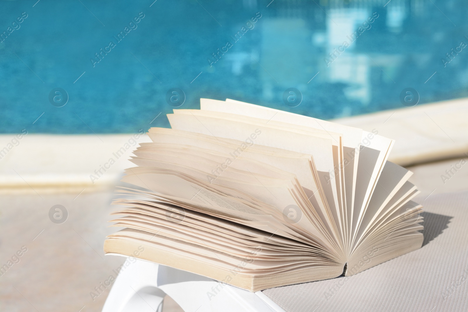 Photo of Open book on deck chair near swimming pool