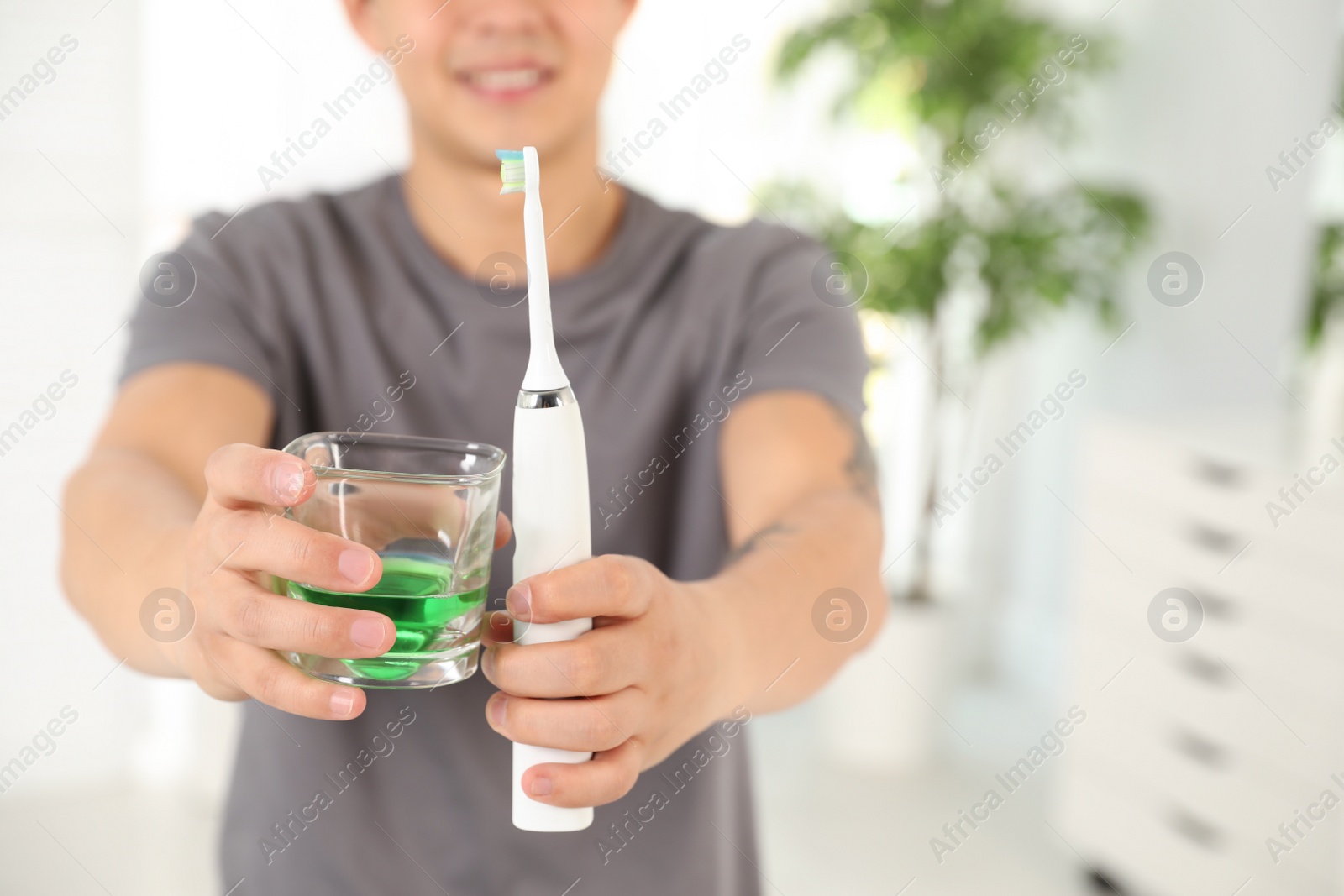 Photo of Man holding glass with mouthwash and toothbrush in bathroom, closeup. Teeth care