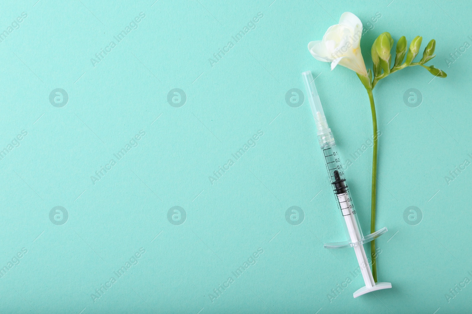 Photo of Cosmetology. Medical syringe and freesia flower on turquoise background, top view. Space for text