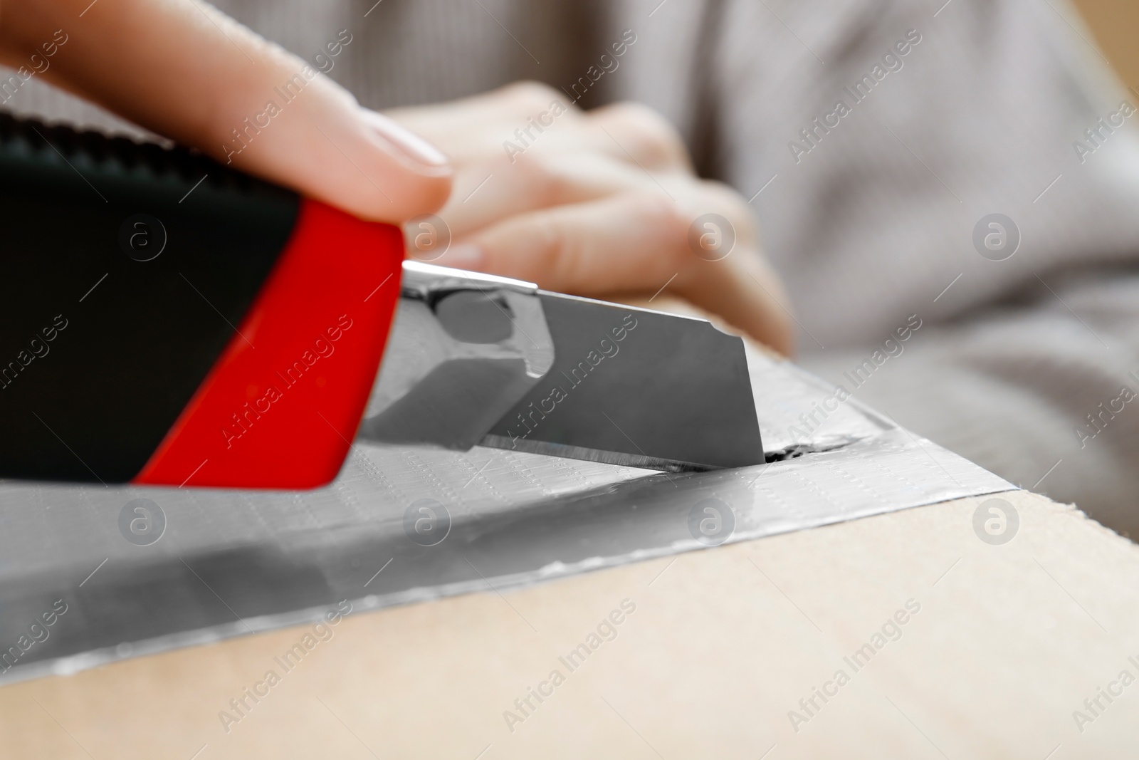 Photo of Woman using utility knife to open parcel, closeup