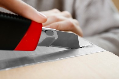 Woman using utility knife to open parcel, closeup